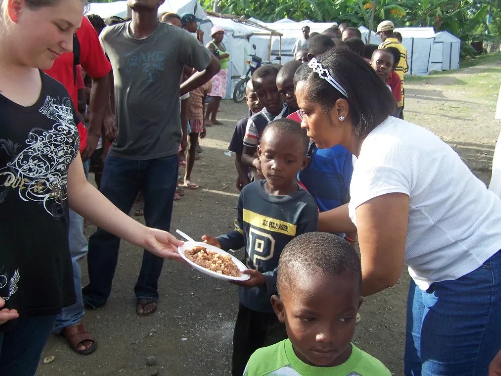 A woman handing food to a child in front of other people.