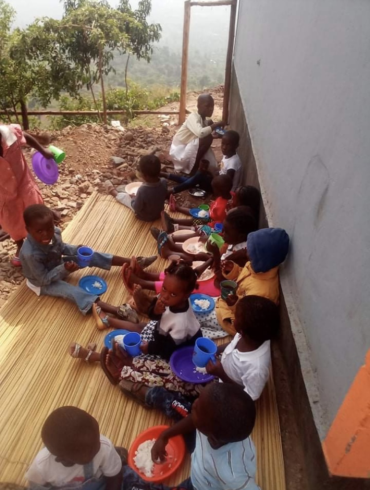 A group of children sitting on the ground eating food.